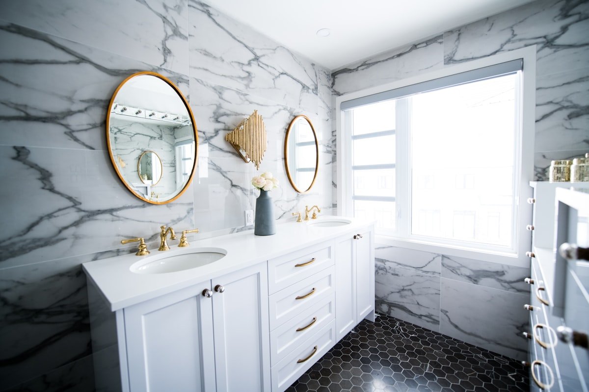 Remodeled bathroom with marble walls, double vanity and brass fixtures
